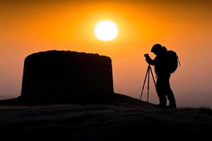 A man with a backpack and a tripod is taking a picture of the sunset photo