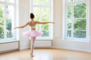 A young ballerina in a pink tutu is standing in front of a large window photo