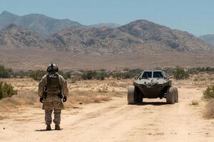 A soldier standing in the middle of a desert road with a vehicle photo