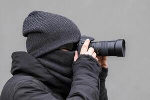 A man wearing a winter hat and a black mask is taking a photo