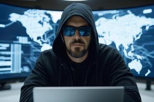 A man in a hoodie and sunglasses is using a laptop photo