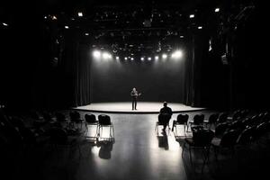 A man stands in front of a stage with chairs photo