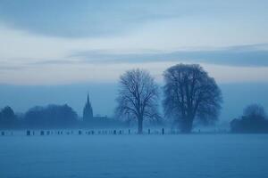 A foggy morning in a field with trees and a church photo