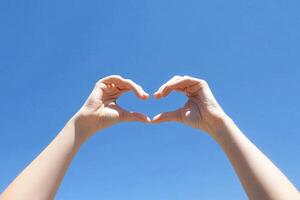 Hands making heart shape with blue sky background photo