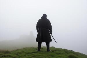 A man in a black cloak stands on a hill with a sword photo