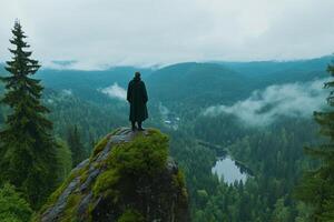 Man standing on top of a mountain overlooking a forest photo
