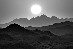 Black and white photo of the sun setting over mountains
