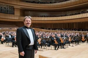 A man in a tuxedo standing in front of an orchestra photo