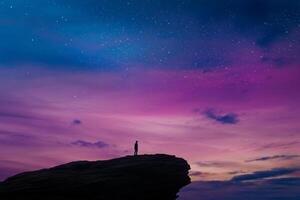 Man standing on top of a cliff looking at the sky photo