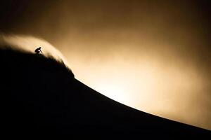 A person riding a snowboard down a mountain at sunset photo