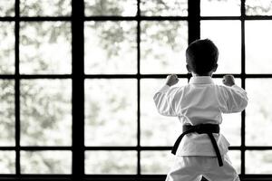 A young boy in karate gear standing in front of a window photo