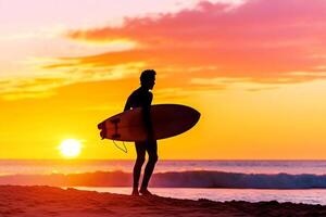 A man standing on the beach holding a surfboard at sunset photo