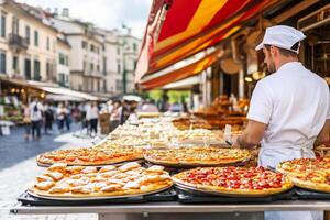 A man in a white hat is standing in front of a table with many pizzas photo