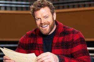 A man in a red plaid jacket is smiling and holding a piece of paper photo