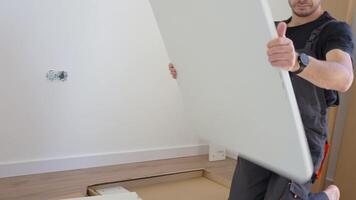 Man assembles furniture panel near unpacked parts and tools at home. Handyman preparing part of bed for assembly in bedroom video