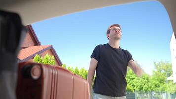Man placing orange rolling suitcase into open vehicle trunk video