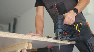 Man in workwear using jigsaw to cut chipboard panel in modern home workshop video