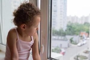 Curly child looks out the window sitting on the windowsill photo