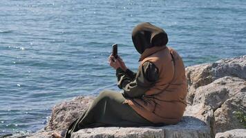 Person using smartphone by the water in sunny weather video