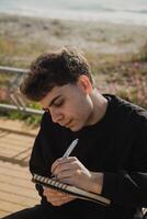 College Student Writing Notes And Studying On A Bench Near The Ocean photo