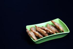 A green dish featuring fried chicken atop Aloo Puff Pastry, served with a side of tomato sauce. photo