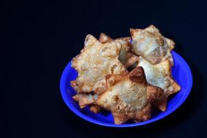 A blue plate holds Aloo Puff Pastry served with a side of tomato sauce. photo