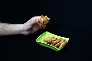 A hand presents a green dish containing Aloo Puff Pastry, accompanied by a small bowl of tomato sauce. photo