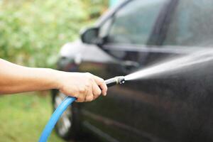 Closeup of a hand holding a gun pipe to spray high-pressure water onto a car during washing. This represents equipment used in car care, self-service washing, and regular car maintenance. photo