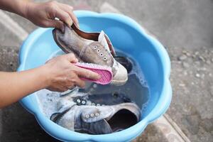 Close up hands use washing brush to scrub sneakers during soak in detergent water in bowl. Concept, footwear cleaning. Get rid of stain and dirt on shoes for sanitary. photo