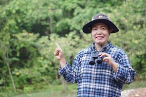 Asian woman botanist, hold binoculars, point and smile. Concept, forest exploration. Environment conservation. Go hiking. Hobby and lifestyle. photo