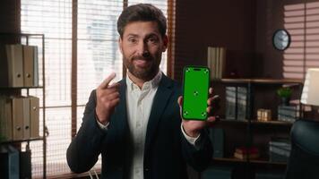 souriant content milieu vieilli affaires homme montrant vert écran mobile téléphone montrer du doigt doigt sur téléphone intelligent chrominance clé afficher pari casino application mature homme d'affaire Masculin à la recherche à caméra dans Bureau video