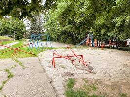 Empty retro playground with seesaws, swings, and a slide under green trees. A quiet and nostalgic public space in the city. photo