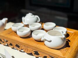 White teaware set on carved wooden tray. Porcelain bowls and pitchers arranged for traditional tea preparation. photo
