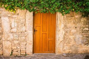 Wooden door framed by ivy and ancient stone wall. Summer travel, rustic charm, and the warmth of Mediterranean architecture in small historic towns. Copy space photo