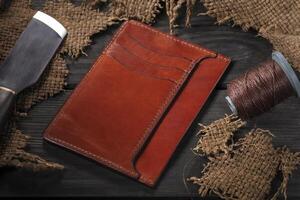 Making leather wallets. On a wooden table there is a wallet, a spool of thread and a knife. photo