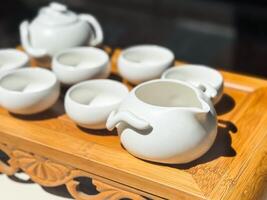 Porcelain bowls and pitchers arranged for traditional tea preparation. White teaware set on carved wooden tray. photo