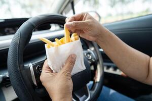 lady holding French fries potato chips to eat in car, dangerous and risk an accident. photo
