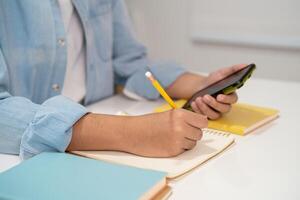 Teenage write in notebook and use mobile phone search data online to online learning photo
