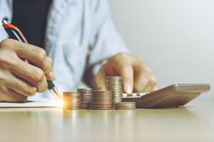 Businessman working using calculator with Money coins for Plans to Accountancy on wood table stack in office at home, Front view with copy space. Accounting and financial economic calculation concepts photo