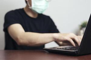 Asian man Wear a mask to protect against Corona virus. working at home, Doing work using a laptop, data keys, Online marketing. Focus on the edge of the laptop screen, blurred background for content photo
