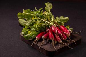 Vibrant red radishes with lush green leaves sit on a dark wooden cutting board, creating a simple yet appealing display of fresh produce photo