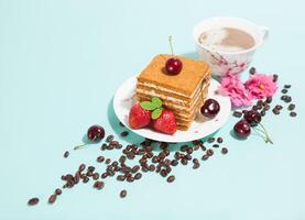 Tasty piece of cake on the white plate and cup of coffee,decorated with flowers,coffee beans,strawberries and cherry on the light mint background with empty place,perspective view,diagonal composition photo