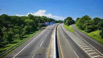 High-angle view of a well-maintained multi-lane highway, bordered by verdant trees, with a clear blue sky and distant road signs photo