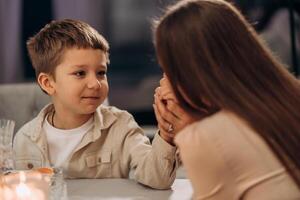 Calm and loving boy holds his mothers hands while looking into her eyes across candlelit dinner table capturing a quiet moment of trust support and affection ideal for Valentines family concept or photo