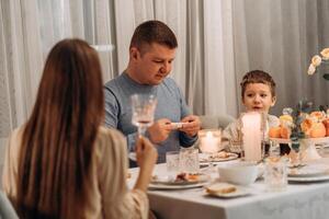 Father and son share thoughtful dinner moment at cozy table with candles fruit and flowers while mother listens from foreground capturing authentic family interaction warmth connection and mindful photo
