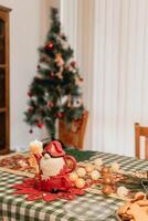 Warm cozy Christmas atmosphere with a Santa teapot and candlelit table full of festive details including garlands pine branches cookies and a tree glowing gently in the soft seasonal background photo