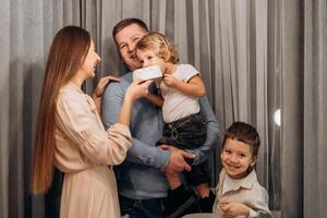 Happy young family celebrates laughter as toddler bites into white cake while being held by smiling father and surrounded by joyful mother and sibling during emotional cozy moment shared togetherness photo