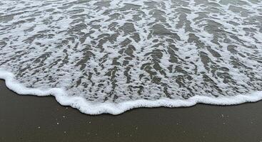 Close-up of ocean waves with white foam washing onto dark sand at the shoreline photo