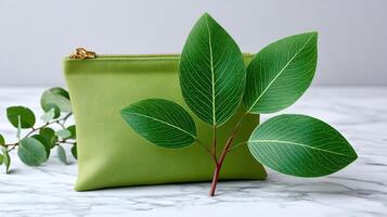 Green cosmetic bag with golden zipper and eucalyptus leaves on marble table photo