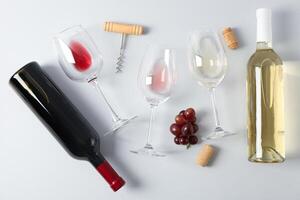 Flat lay. Grapes, corkscrew, bottles and glasses with wine on grey background photo